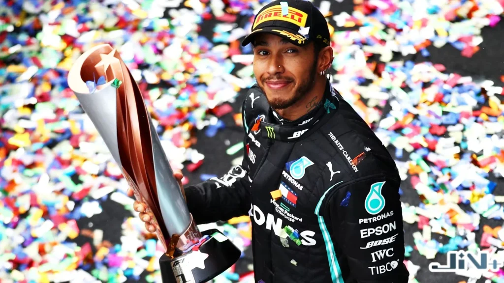 漢米爾頓（Lewis Hamilton）手持冠軍獎盃，同為 7 次 F1 世界冠軍次數保持者與 F1 車手薪資排名榜首。