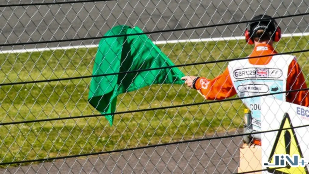F1綠旗安全通行指示，賽道工作人員在綠色草皮護欄旁揮舞綠色旗幟，宣告危險解除。