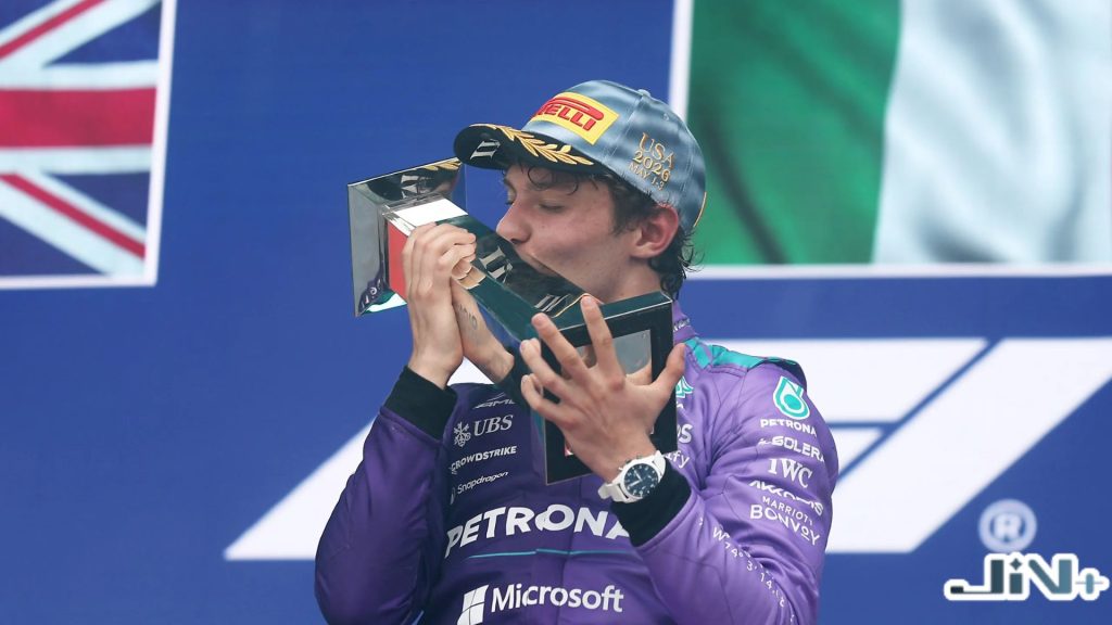 Kimi Antonelli首勝奪冠高光畫面，身穿紫色賽車服在頒獎台上激情親吻分站冠軍獎盃，背景高掛英國國旗。